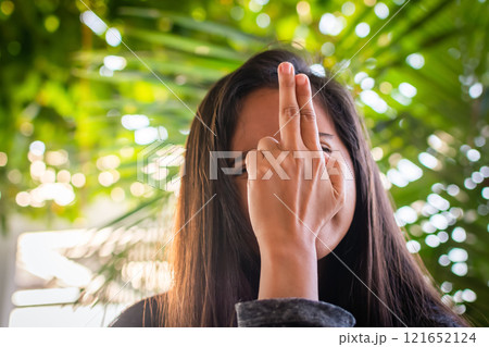 A young woman is showing a finger gun against a palm leaves. fingers folded in the shape of a gun A young woman is showing a finger gun against a palm leaves. fingers folded in the shape of a gun 121652124
