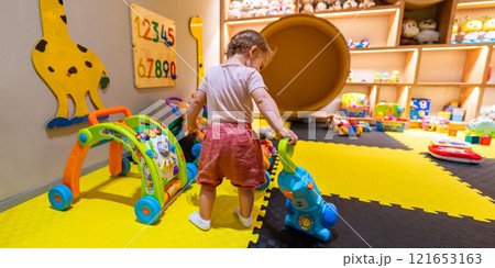 Child using a toy vacuum cleaner for pretend cleaning in a vibrant playroom with interactive learning toys 121653163