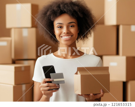 Smiling young woman holding a smartphone, credit card, and package 121653315