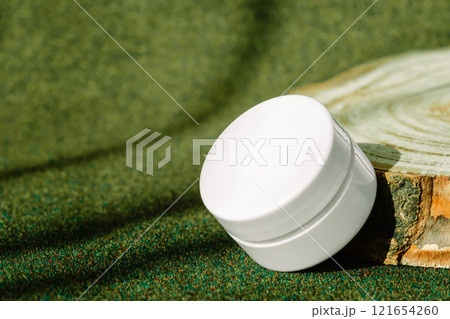 Jar of firming cream with collagen placed on round wooden display on green earthy toned background 121654260