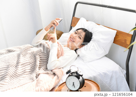 ベッドでスマホを持つ笑顔のアジア人女性 121656104