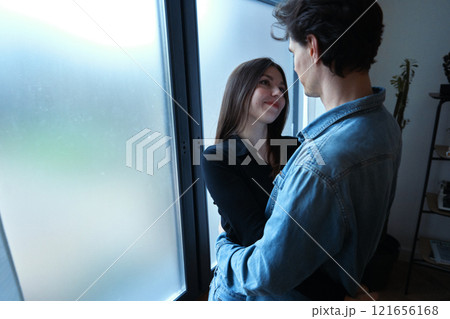 Young couple sharing a tender moment indoors by a window during daylight 121656168