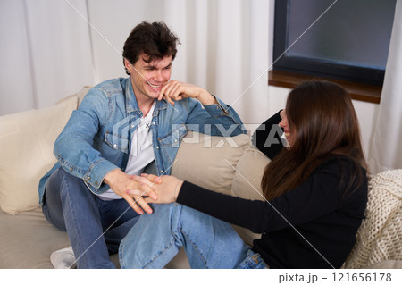 Young couple enjoying a playful moment together on a cozy sofa indoors 121656178