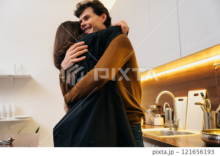 Happy couple embraces in modern kitchen during cozy evening together Happy couple embraces in modern kitchen during cozy evening together 121656193