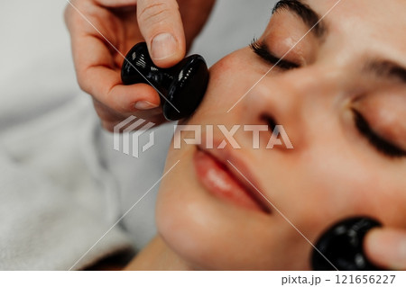 Woman receiving facial treatment with tools at a wellness spa during daytime Woman receiving facial treatment with tools at a wellness spa during daytime 121656227