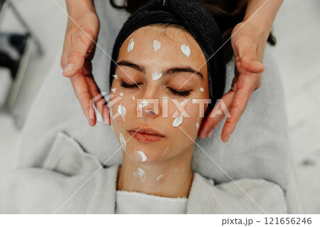 Relaxing spa treatment for young woman with facial cream at wellness center in modern salon Relaxing spa treatment for young woman with facial cream at wellness center in modern salon 121656246
