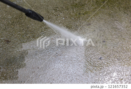 Woman cleaning concrete pavement using high pressure washer. 121657352