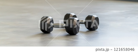 Two black dumbbells on a gym floor, promoting fitness and strength training. Metal and rubber grips hint at muscle building potential. Ideal for weightlifting and bodybuilding messages 121658046