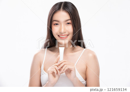 Beautiful Asian woman with a radiant smile holding a blank tube, ready for your cosmetic or skincare branding. Confidence and elegance personified isolated on white background. Self Care Concept Beautiful Asian woman with a radiant smile holding a blank tube, ready for your cosmetic or skincare branding. Confidence and elegance personified isolated on white background. Self Care Concept 121659134