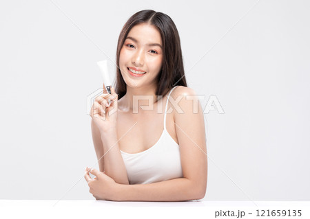 Beautiful Asian woman with a radiant smile holding a blank tube, ready for your cosmetic or skincare branding. Confidence and elegance personified isolated on white background. Self Care Concept 121659135