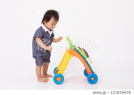 curious Asian toddler wearing a blue outfit with white collar playing with colorful push walker toy. The child focused on exploring the toy showcasing an early learning and development moment 121659479