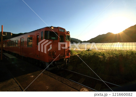 夕日を受けながら出発する列車 121660082