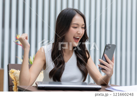Millennial asian young woman looking mobile phone laughing with good news or discount voucher for shopping online at home.Happy and cheerful woman looking on cellphone app read message feel excited 121660248