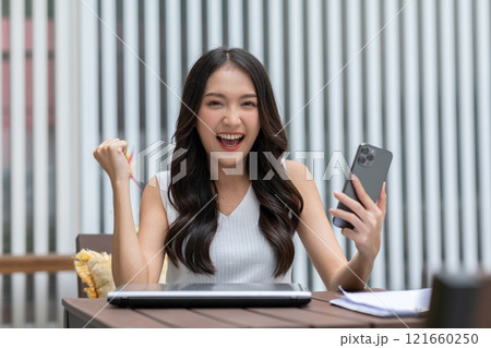 Millennial asian young woman looking mobile phone laughing with good news or discount voucher for shopping online at home.Happy and cheerful woman looking on cellphone app read message feel excited 121660250