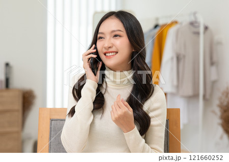 A cheerful young woman converses on her smartphone, radiating joy and confidence in a bright, stylish environment. 121660252