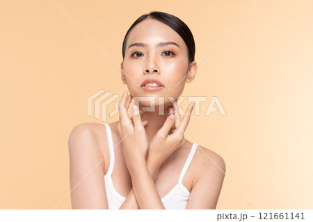 A beautiful woman poses elegantly against a soft orange background, showcasing her flawless skin and serene expression. 121661141