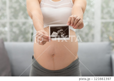 Close up Happy Pregnant Woman holding ultrasound image stroking big belly with love isolated on couch,Pregnancy of young woman enjoy with future life,Motherhood and Pregnant Concept 121661397