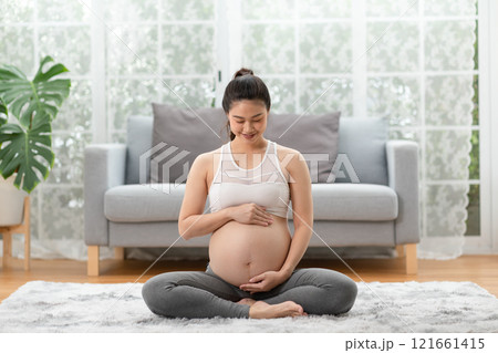 Happy Pregnant Asian Woman sitting on bed holding and stroking her big belly at home,Pregnancy of young woman enjoying with future life relax at home,Motherhood and Pregnant Concept,Soft focus 121661415