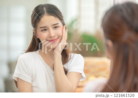 Asian Woman Admiring Smooth Skin in Mirror During Skincare Routine 121661520