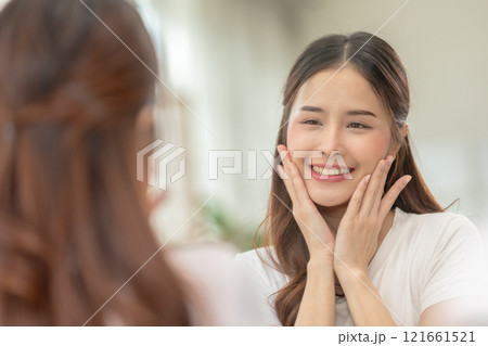Asian Woman Admiring Smooth Skin in Mirror During Skincare Routine 121661521