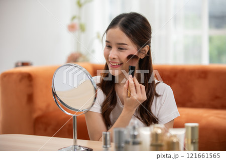 Happy Asian young woman smile and looking in mirror doing skin care applying make up brush on her cheek and beauty treatment at home,Wellness woman self care with beauty product at home 121661565