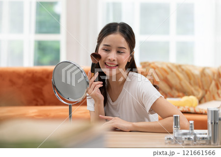 Happy Asian young woman smile and looking in mirror doing skin care applying make up brush on her cheek and beauty treatment at home,Wellness woman self care with beauty product at home 121661566