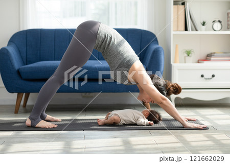 Side view of Wellness Asian woman mom doing yoga Downward Facing dog with baby at cozy home.Happy healthy mother yoga exercise newborn baby boy sleep and lying at warmth place. Mom and Baby Concept 121662029