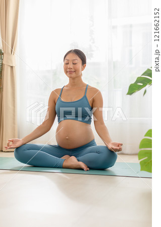 Pregnant woman practicing prenatal yoga at home, focusing on relaxation and mindfulness in a tranquil setting. Pregnant woman practicing prenatal yoga at home, focusing on relaxation and mindfulness in a tranquil setting. 121662152
