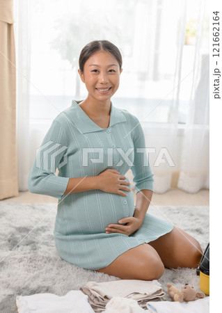 Pregnant woman sitting on the floor at home in a serene and bright room, embracing her belly with a joyful expression. 121662164