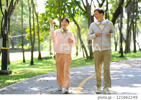 Happy an older man and his daughter enjoying their exercise routine, jogging together through a park path Happy an older man and his daughter enjoying their exercise routine, jogging together through a park path 121662249