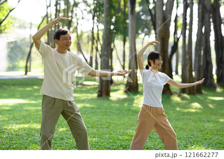 Calm middle aged man and young woman practicing Tai Chi standing in graceful poses on mats in picturesque park 121662277