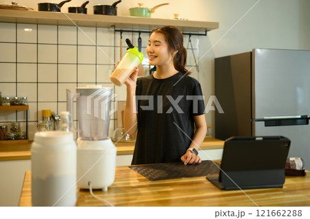 Happy young woman drinking chocolate protein shake in a modern kitchen Happy young woman drinking chocolate protein shake in a modern kitchen 121662288