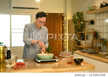 Middle aged man preparing a delicious meal with fresh ingredients in a kitchen Middle aged man preparing a delicious meal with fresh ingredients in a kitchen 121662308