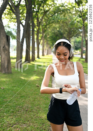 Fit young African woman monitoring her exercise progress on a smartwatch while jogging outdoors Fit young African woman monitoring her exercise progress on a smartwatch while jogging outdoors 121662356