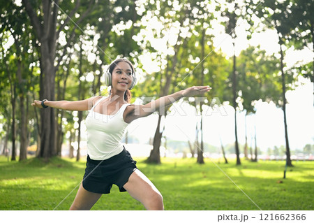 Attractive fit woman wearing headphone practicing yoga on a grassy lawn. Healthy lifestyle concept Attractive fit woman wearing headphone practicing yoga on a grassy lawn. Healthy lifestyle concept 121662366