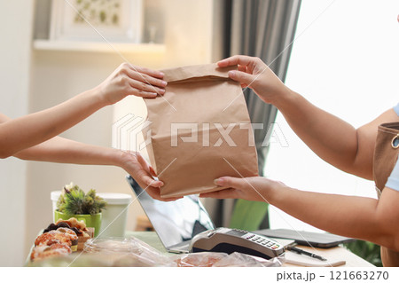 close up shot capturing moment customer receives brown paper bag from chef during a food exchange. focuses on the hands holding the bag, symbolizing the personal touch and care in food service 121663270