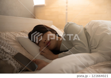 スマホを見ながら寝落ちしてしまった女性 黄色い間接照明 スマホを見ながら寝落ちしてしまった女性 黄色い間接照明 121664021