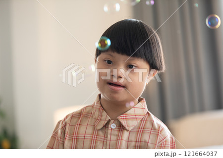 Asian cheerful young boy with Down syndrome enjoys playing with bubbles indoors. His bright smile and playful gestures capture the innocence and joy of childhood 121664037