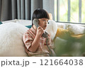 Asian young boy with Down syndrome sits comfortably at home, engaged in a phone conversation. He holds a retro-style telephone, focusing intently on the call 121664038