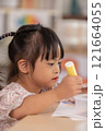Asian young girl with Down syndrome wearing pigtails, is immersed in arts and crafts project at table. She holds piece of colored paper with focus and concentration, surrounded by crafting materials 121664055