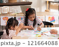 Two young Asian girls with Down syndrome engage in a fun arts and crafts activity, sharing smiles and creativity. They are focused on crafting with colorful materials 121664088