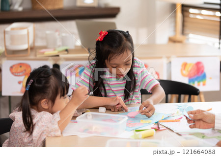 Two young Asian girls with Down syndrome engage in a fun arts and crafts activity, sharing smiles and creativity. They are focused on crafting with colorful materials 121664088