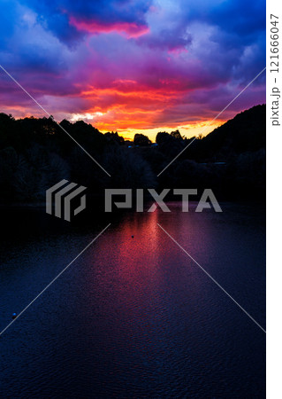 新春の奈良布目ダム寒風吹きすさぶ夕景　紺色の空と湖面に囲まれた燃えるような夕焼けの空と湖面② 121666047