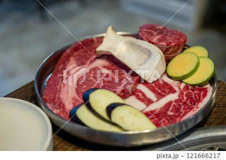 A close-up shot of premium cuts of marbled Hanwoo beef placed on a metal tray, with sliced eggplant and zucchini and eryngii mushroom A close-up shot of premium cuts of marbled Hanwoo beef placed on a metal tray, with sliced eggplant and zucchini and eryngii mushroom 121666217
