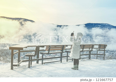 A serene winter scene showing a person capturing a picturesque snowy mountain view with a camera 121667757
