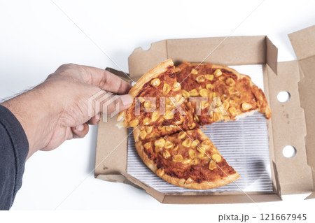 Hand holding a pizza slice from a box with corn topping 121667945