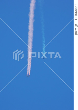 快晴の空を煙幕を引きながらパラシュートで降下する人々 121668832