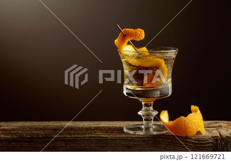 Old Fashioned cocktail in a crystal glass garnished with an orange peel on a old wooden board. Old Fashioned cocktail in a crystal glass garnished with an orange peel on a old wooden board. 121669721