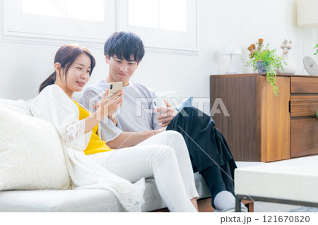 リビングでスマホを見る若い夫婦 リビングでスマホを見る若い夫婦 121670820