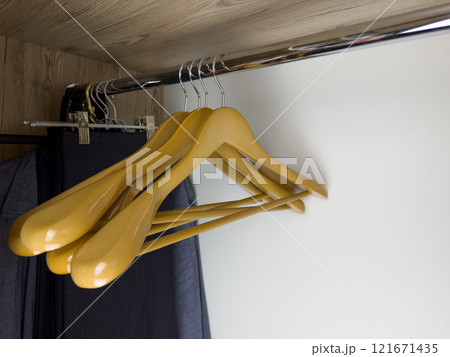 Set of convenient light wood hangers hanging on beam inside clothes closet at home, hangers in closet without clothes, storing clean clothes at home Set of convenient light wood hangers hanging on beam inside clothes closet at home, hangers in closet without clothes, storing clean clothes at home 121671435